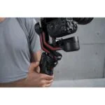 Person holding DJI RS 3 gimbal stabilizer with camera attached.