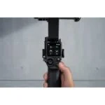 Hand holding DJI RS 3 gimbal stabilizer with control screen visible.