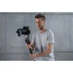 Man using DJI RS 3 gimbal stabilizer with camera in a studio setting.