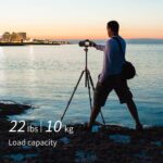 Photographer using a tripod by the sea at sunset, showcasing camera gear.