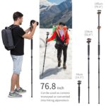 Man using a camera monopod while hiking, with a woman in the background on a snowy mountain.