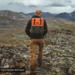 Hiker with orange backpack on rocky mountain trail, scenic view.