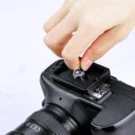 Person inserting coin into camera battery grip for secure attachment.