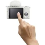 Person interacting with a white Sony digital camera with flip screen.
