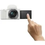 Sony mirrorless camera with flip-out screen and hand interacting, ideal for vlogging and photography.