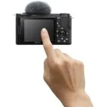 Hand holding a Sony digital camera with a flip screen, ideal for vlogging and photography.