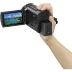 Person holding a Sony camcorder with a flip-out screen displaying a scenic view.