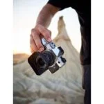 Person holding a mirrorless camera outdoors at sunset.