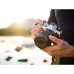 Person holding Olympus mirrorless camera outdoors at sunset.