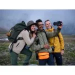 Group of friends taking a selfie with a camera in a scenic outdoor setting.