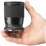 Hand holding Sigma 16mm f/1.4 DC DN lens, ideal for mirrorless cameras.