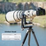 Professional camera with telephoto lens on gimbal head tripod by a lake.