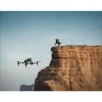 Drone flying near a cliff with a person on horseback, clear sky in the background.