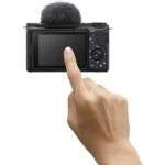 Person interacting with a digital camera's touchscreen, showcasing camera features.