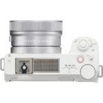 Top view of a white mirrorless camera with lens, featuring control dials and buttons.