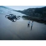 Drone flying over a beach with two people standing in the background.