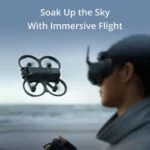 Person flying a drone with VR headset near the ocean.