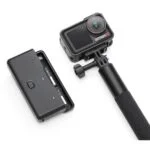 Action camera with selfie stick and battery pack on white background.