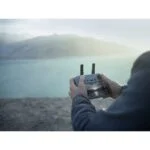 Person operating a drone with a remote control near a scenic landscape.