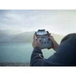 Person using DJI drone controller with smartphone by a lake.