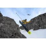 Skier jumping off a snowy cliff with a drone capturing the action.