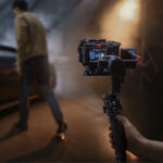 Person using a gimbal with a camera in a dimly lit setting, showcasing photography gear.