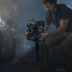 Man using professional camera rig with video camera and accessories in a dimly lit setting.