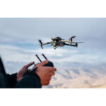 Person flying a DJI drone with remote control in a scenic landscape.