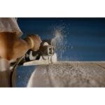 Person using a power tool to sand a surfboard, creating dust.