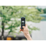 Hand holding a compact digital camera outdoors, showcasing its screen and lens.