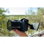 Person holding a Panasonic Lumix camera with a flip-out screen outdoors.