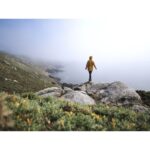Person in yellow jacket standing on rocky cliff overlooking foggy sea