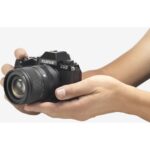 Person holding a Fujifilm X-S10 mirrorless camera with lens.