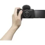 Hand holding a Sony digital camera with flip-out screen, ideal for vlogging and photography.