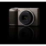 Compact digital camera with lens on black background, available at Camix UK.