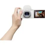 Sony digital camera held in hand, displaying a group selfie on the screen.