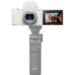 Sony digital camera with flip screen displaying a group photo, mounted on a handheld grip.