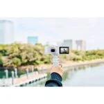 Person holding a white Sony camera with flip screen by a waterfront.