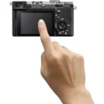 Person interacting with a digital camera's touchscreen, showcasing camera features.