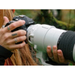 Person holding a professional camera with a large telephoto lens outdoors.