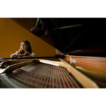 Woman beside a grand piano in a camera shop, showcasing photography equipment.