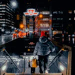 Person entering subway station at night in a city with bright lights.