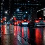 Night city street with cars and reflections, showcasing urban photography.