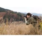Photographer capturing nature with a DSLR camera in a field, showcasing photography gear.