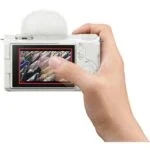 Person holding a white digital camera with a viewfinder display.