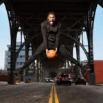 Person jumping with a basketball under a bridge in an urban setting.