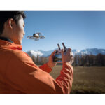 Person flying a drone with remote control in a scenic mountain landscape.