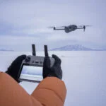 Person flying a drone with remote control in snowy landscape
