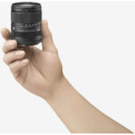 Hand holding Sigma 18-50mm f/2.8 DC DN lens, ideal for mirrorless cameras.