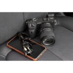 Sony mirrorless camera with lens on car seat, next to smartphone and sunglasses.